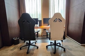 Two gaming chairs facing a desk with a computer monitor, in a room with wooden flooring and large windows. - Le Noble Hotel (Ganzhou City)