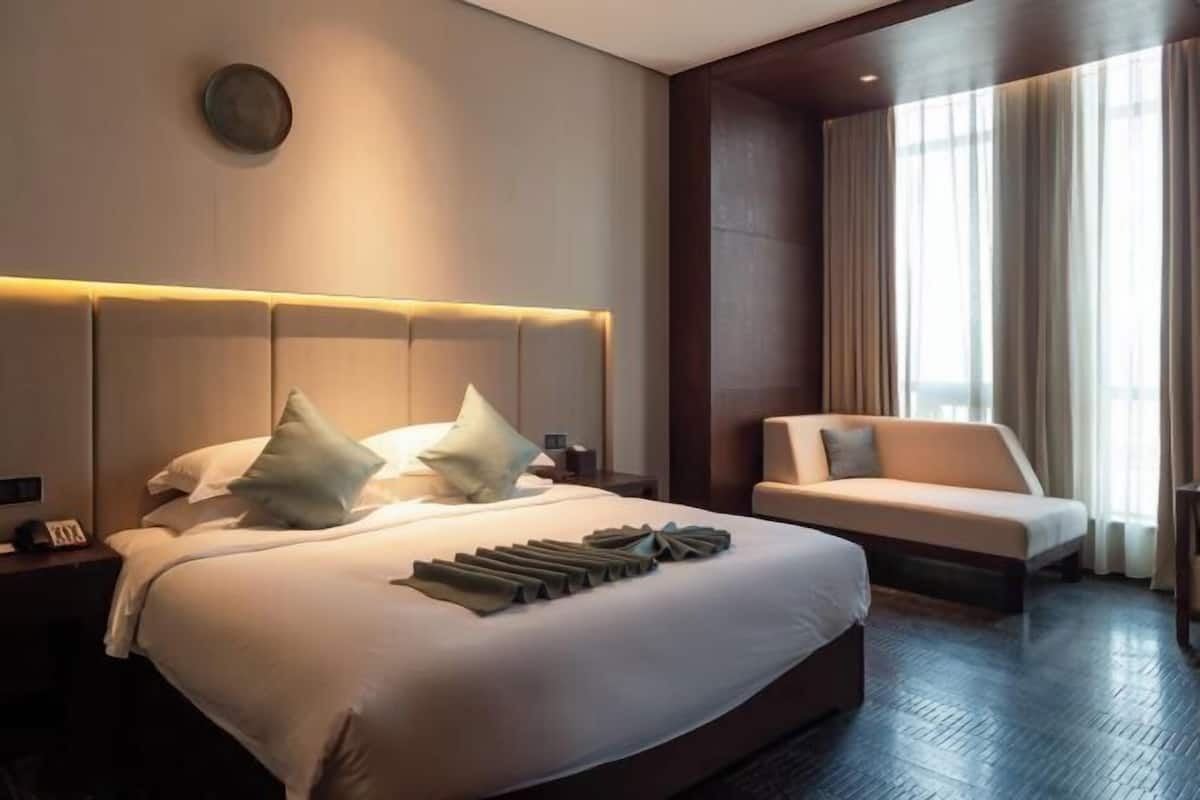 Una habitación de hotel moderna con una cama grande, un sofá y un amplio ventanal con cortinas.