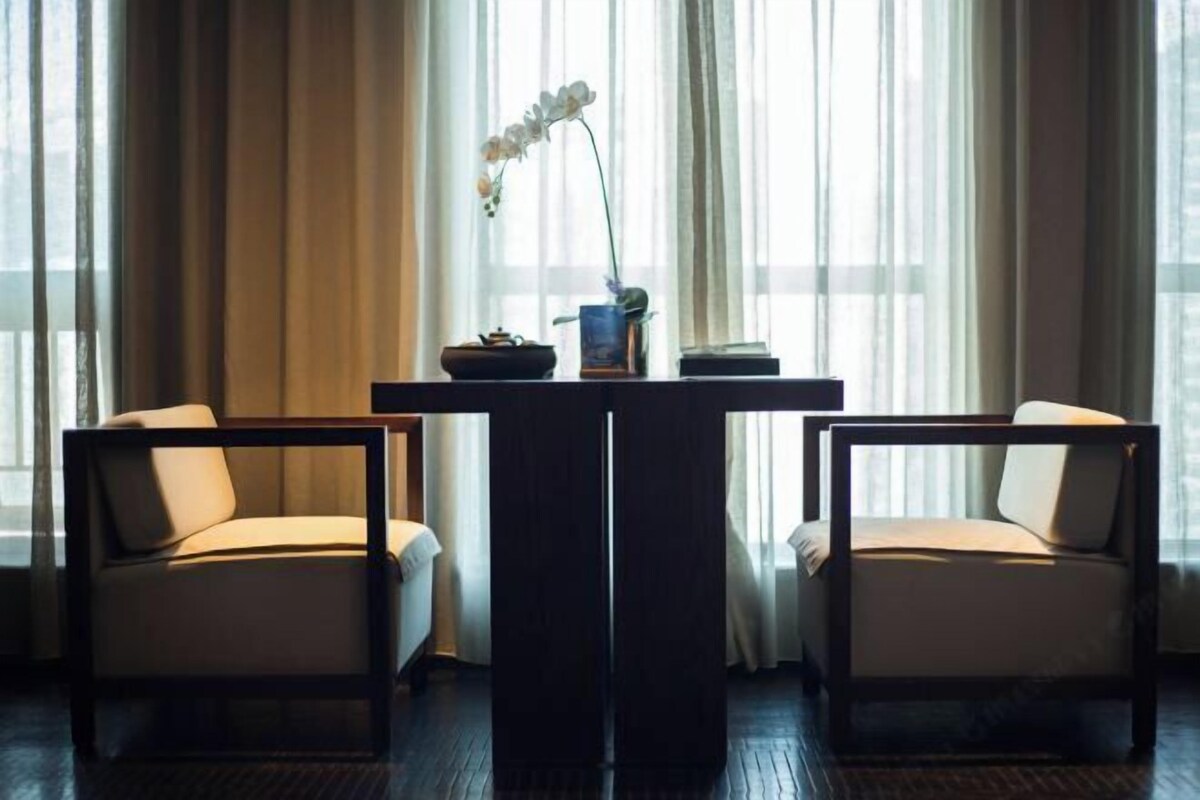 A room with a dark wooden table, two chairs, a vase with flowers, and sheer curtains.