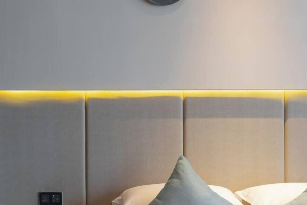 Una habitación de hotel moderna con cabecera acolchada, panel de control y cama con almohadas.