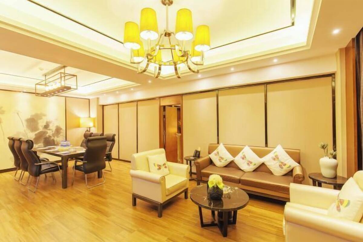 A modern hotel room with a wooden floor, a sofa set, a dining table with chairs, and a chandelier.