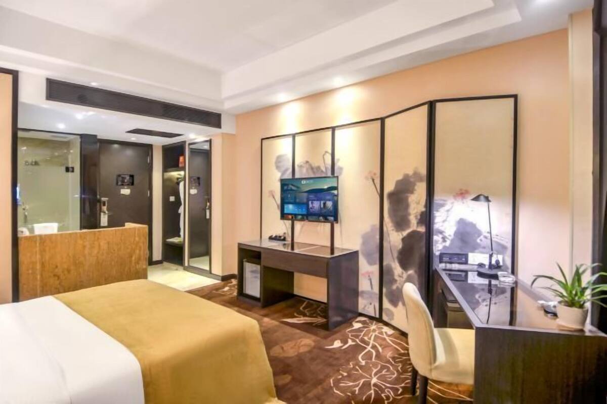 A hotel room with a bed, a desk, a TV, and a mirror.