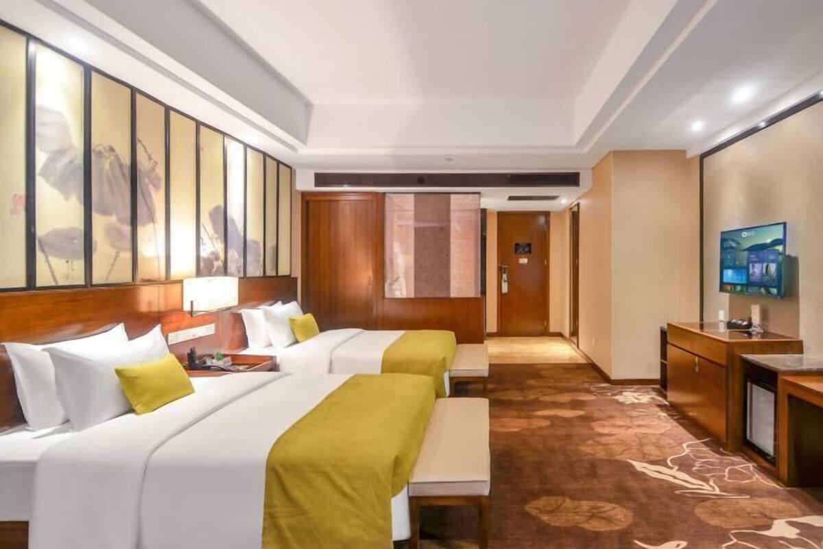 A hotel room with two beds, a desk, a television, and a corridor leading to another room.