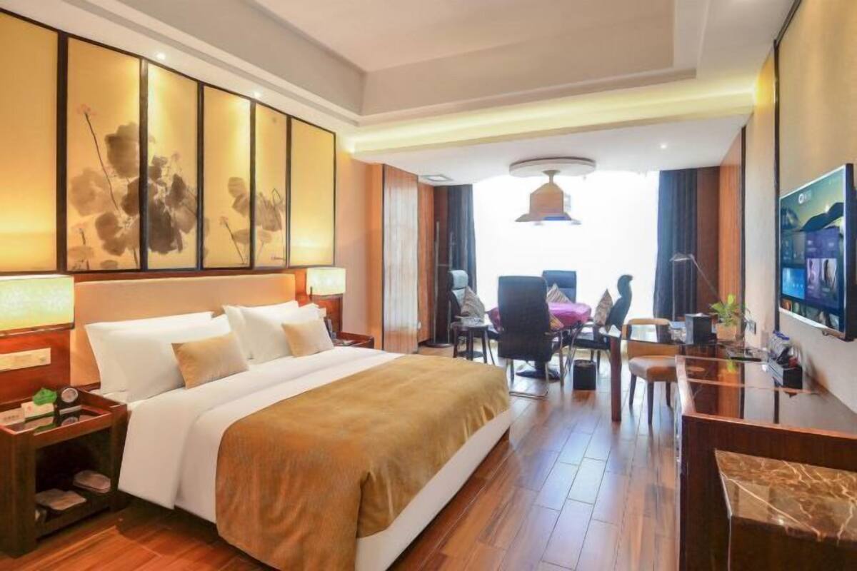 A hotel room with a large bed, a desk with a chair, a television, and artwork on the wall.