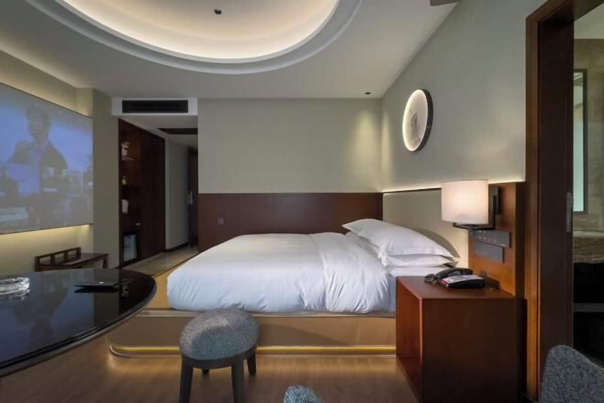 A hotel room with a bed, bedside table, lamp, and a television screen.