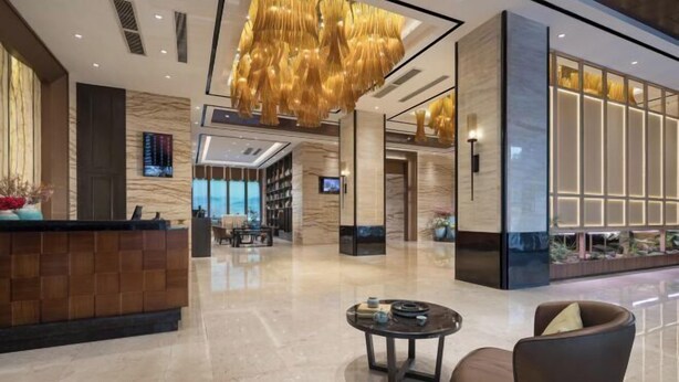 Un moderno vestíbulo de hotel con un mostrador de recepción, área de descanso y una gran lámpara colgante decorativa.
