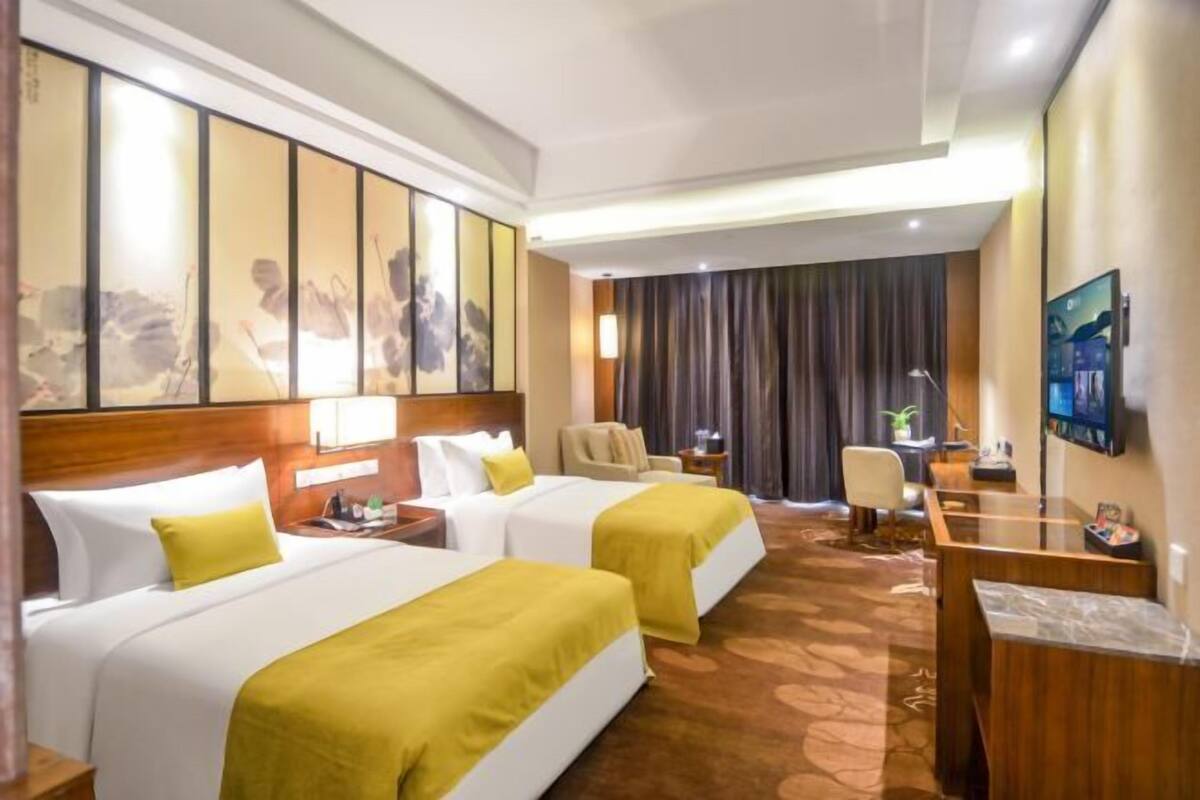 A hotel room with two beds, a desk, a chair, a TV, and a large painting on the wall.