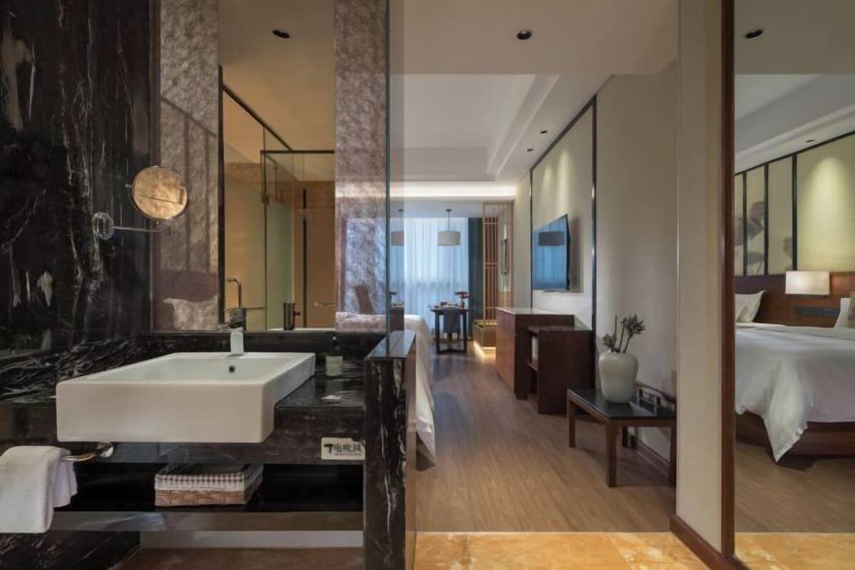A modern hotel room with a large marble bathroom, a bed with a wooden headboard, and a view of the city.
