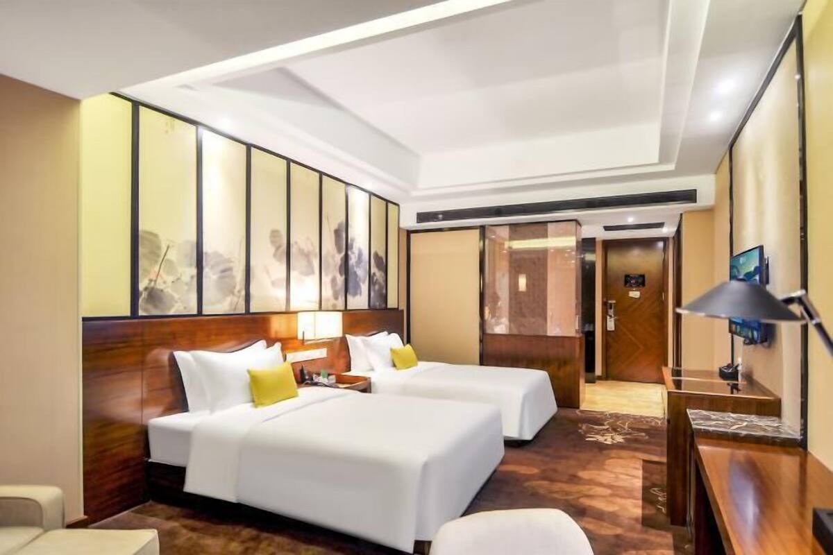 A hotel room with two beds, a desk, a chair, and artwork on the walls.
