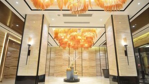 Un vestíbulo moderno con una lámpara decorativa central, paredes de mármol y un diseño simétrico.