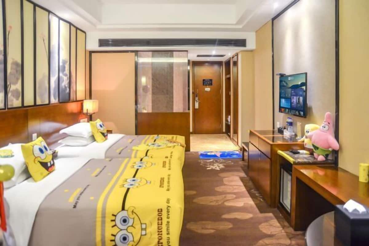 A hotel room with a bed, a desk, a television, and a door.