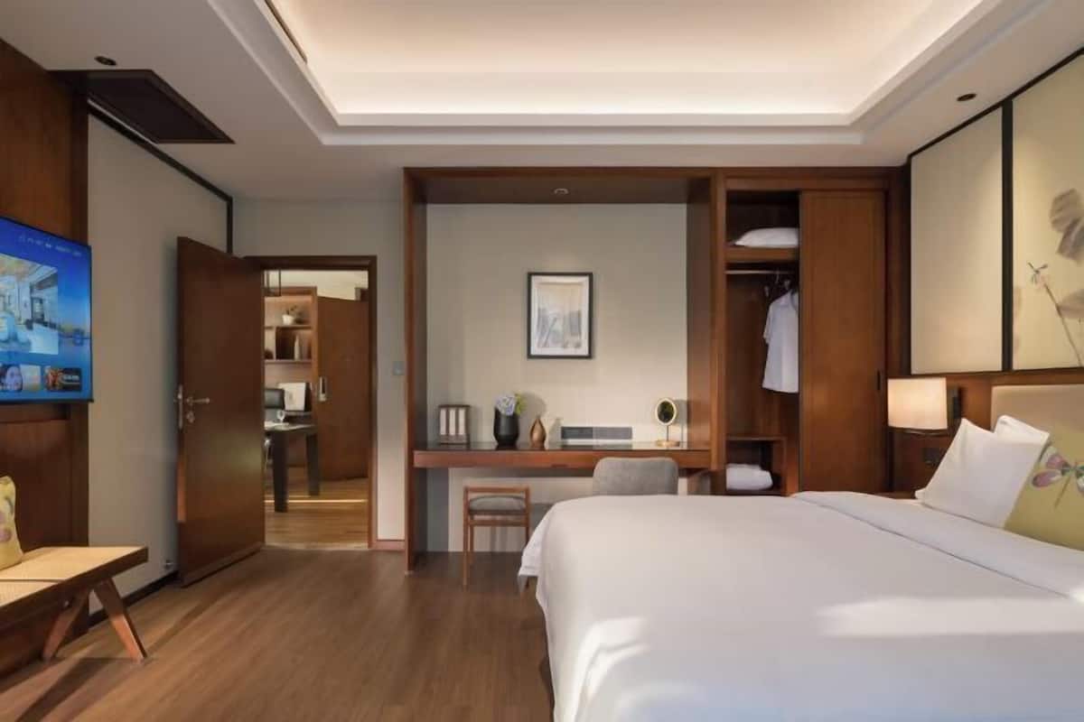 A hotel room with a bed, desk, chair, wardrobe, and a television.