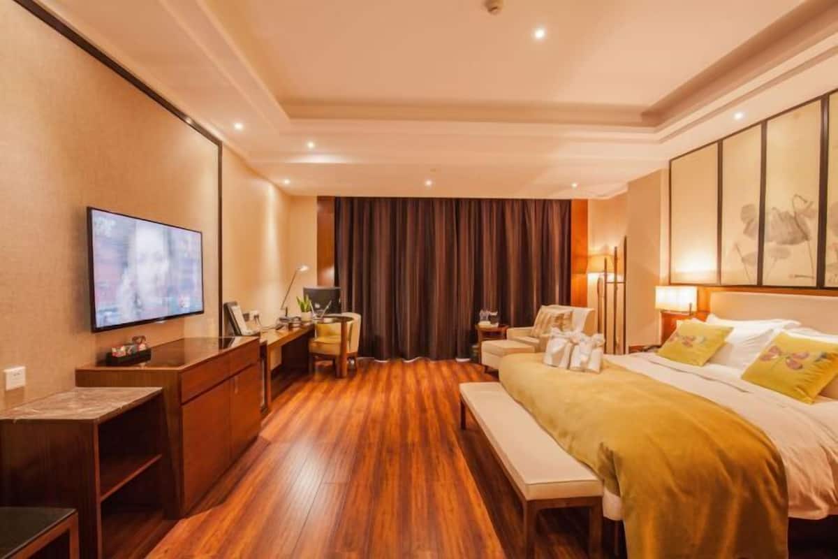 A hotel room with a wooden floor, a bed with yellow bedding, a desk with a computer, a chair, and a TV mounted on the wall.