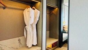 Ein modernes Badezimmer mit Marmorboden, einem weißen Bademantel, der an einem Holzaufhänger hängt, und einem Bett mit weißer Matratze und Kissen.