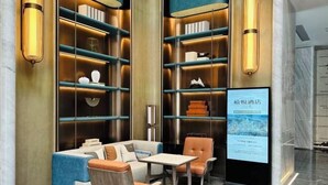 Eine moderne Hotelhalle mit Sitzgelegenheit, Bücherregalen und einem digitalen Bildschirm.