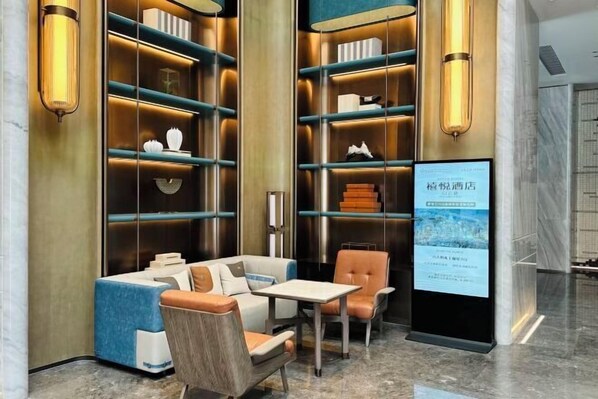 Un lobby moderno de hotel con zona de estar, estanterías y una pantalla digital.
