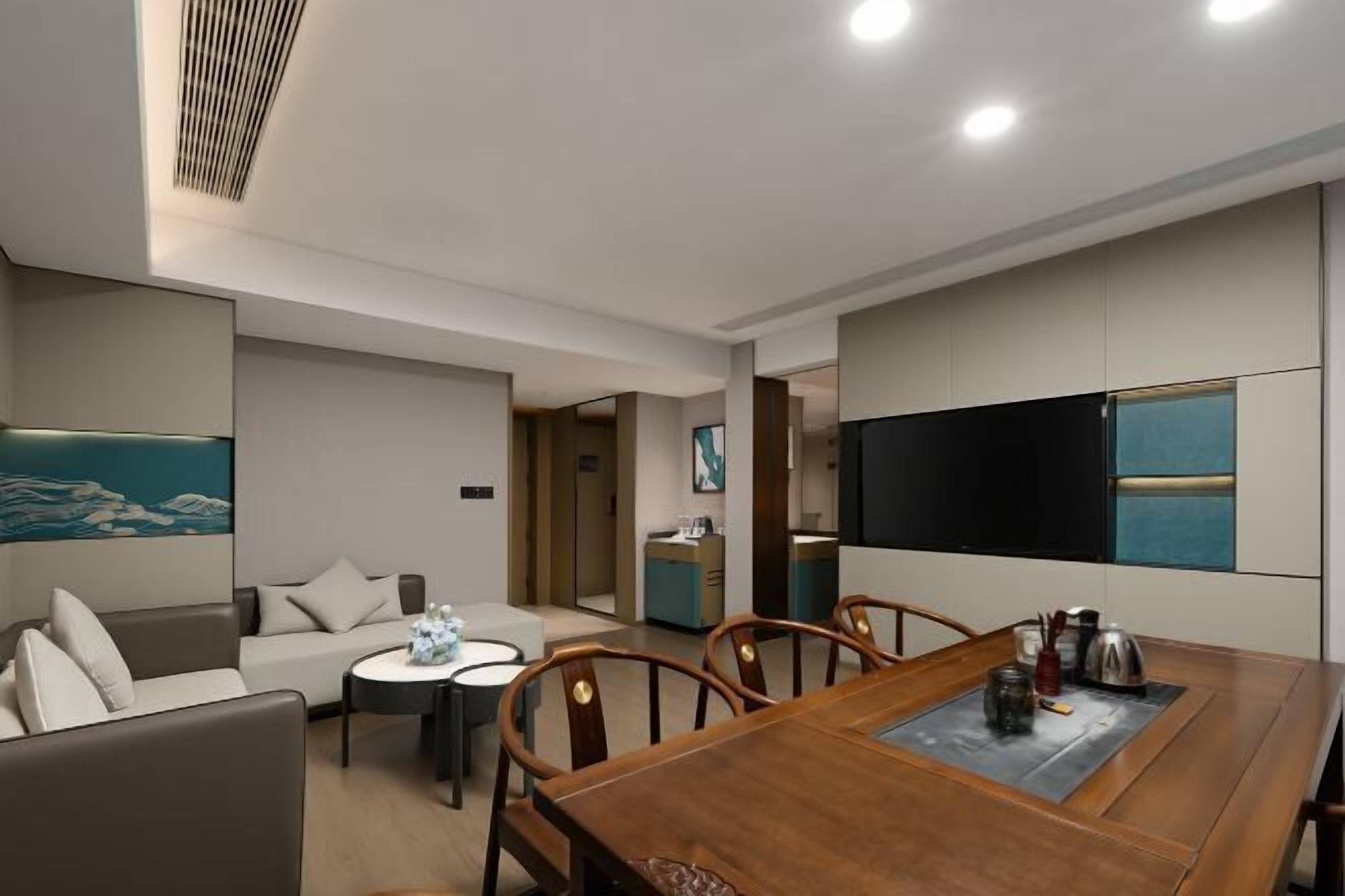 A modern hotel room with a dining area, a sofa, a TV, and a kitchen area.