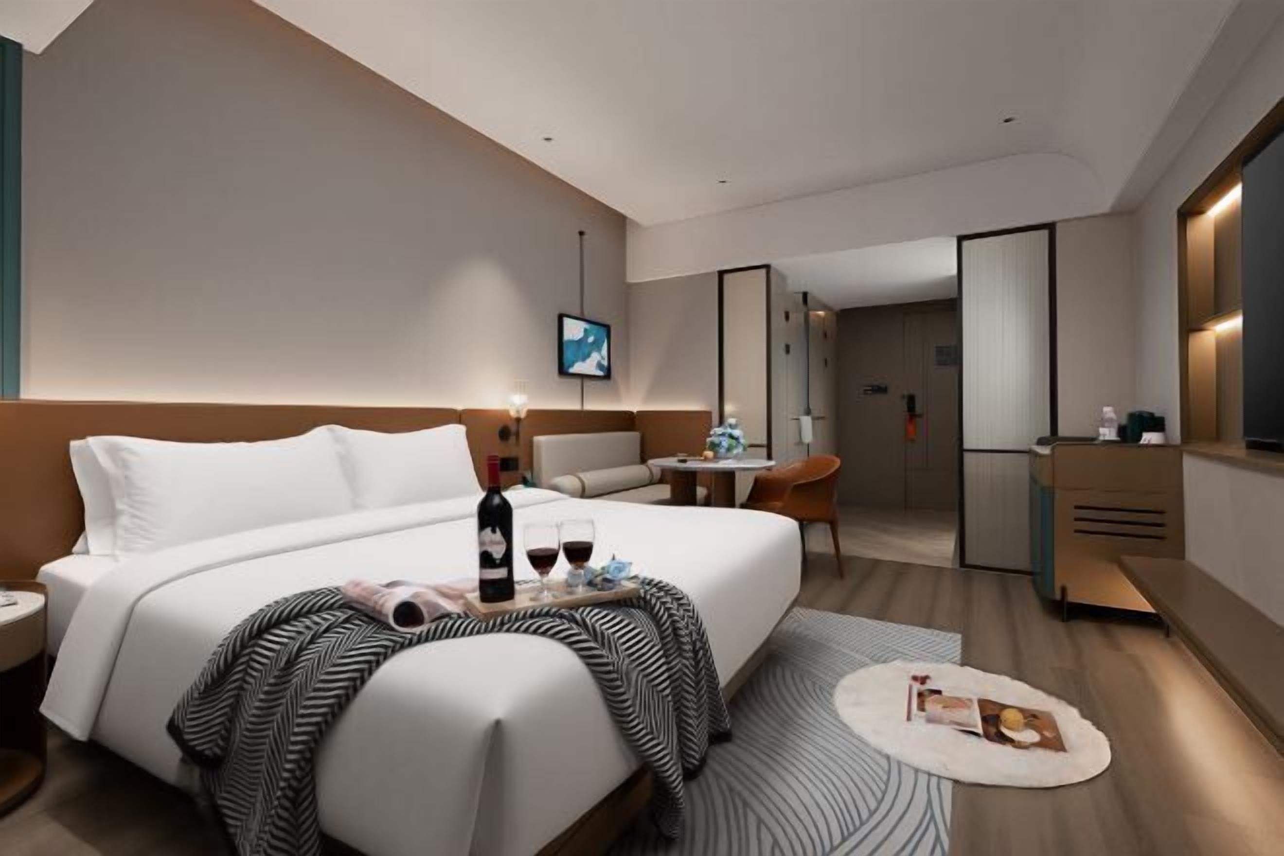 A modern hotel room with a large bed, a desk, a chair, and a TV.