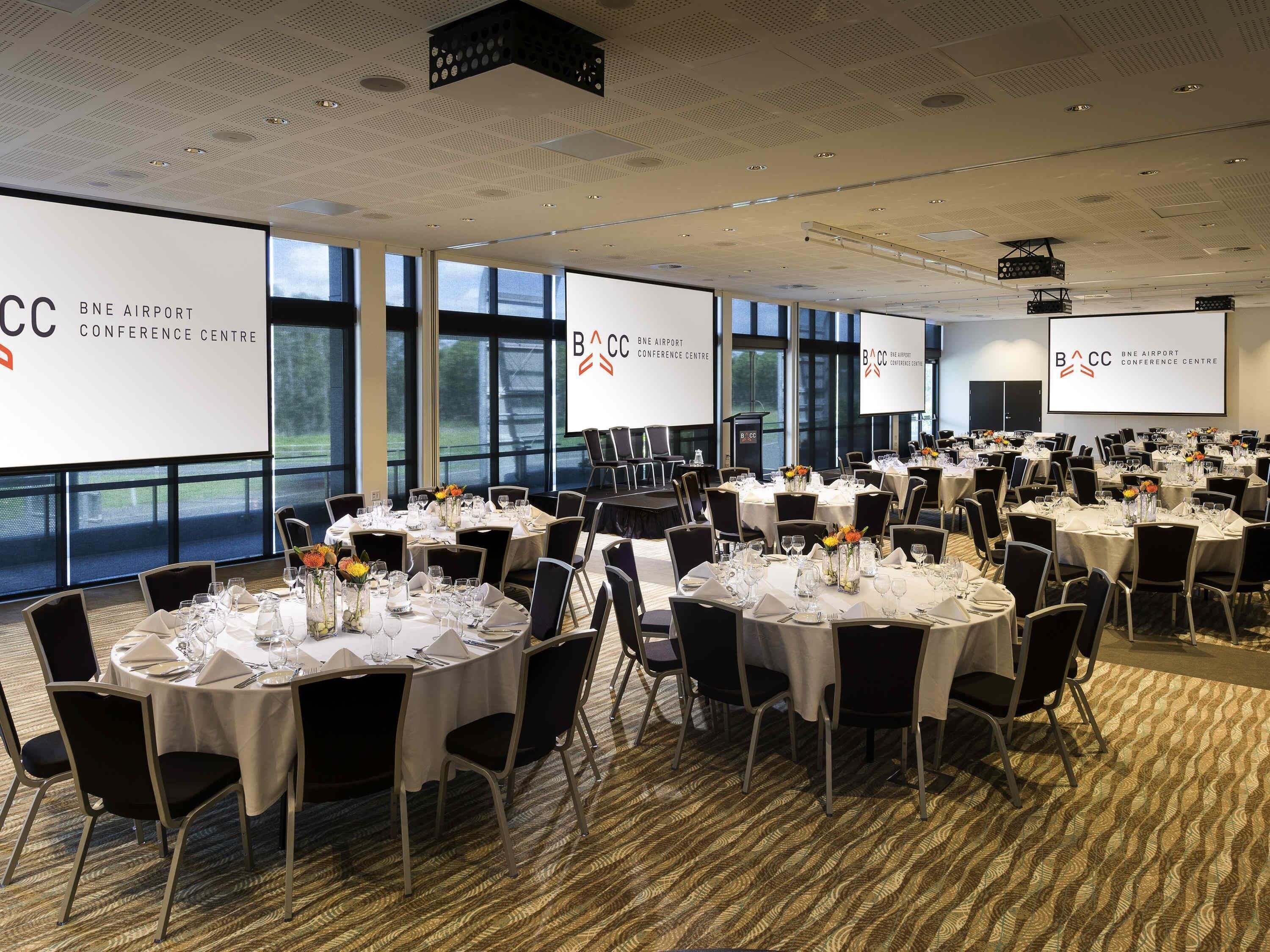 Een congrescentrum met ronde tafels, zwarte stoelen en grote ramen.