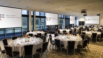 Een congrescentrum met ronde tafels, zwarte stoelen en grote ramen.