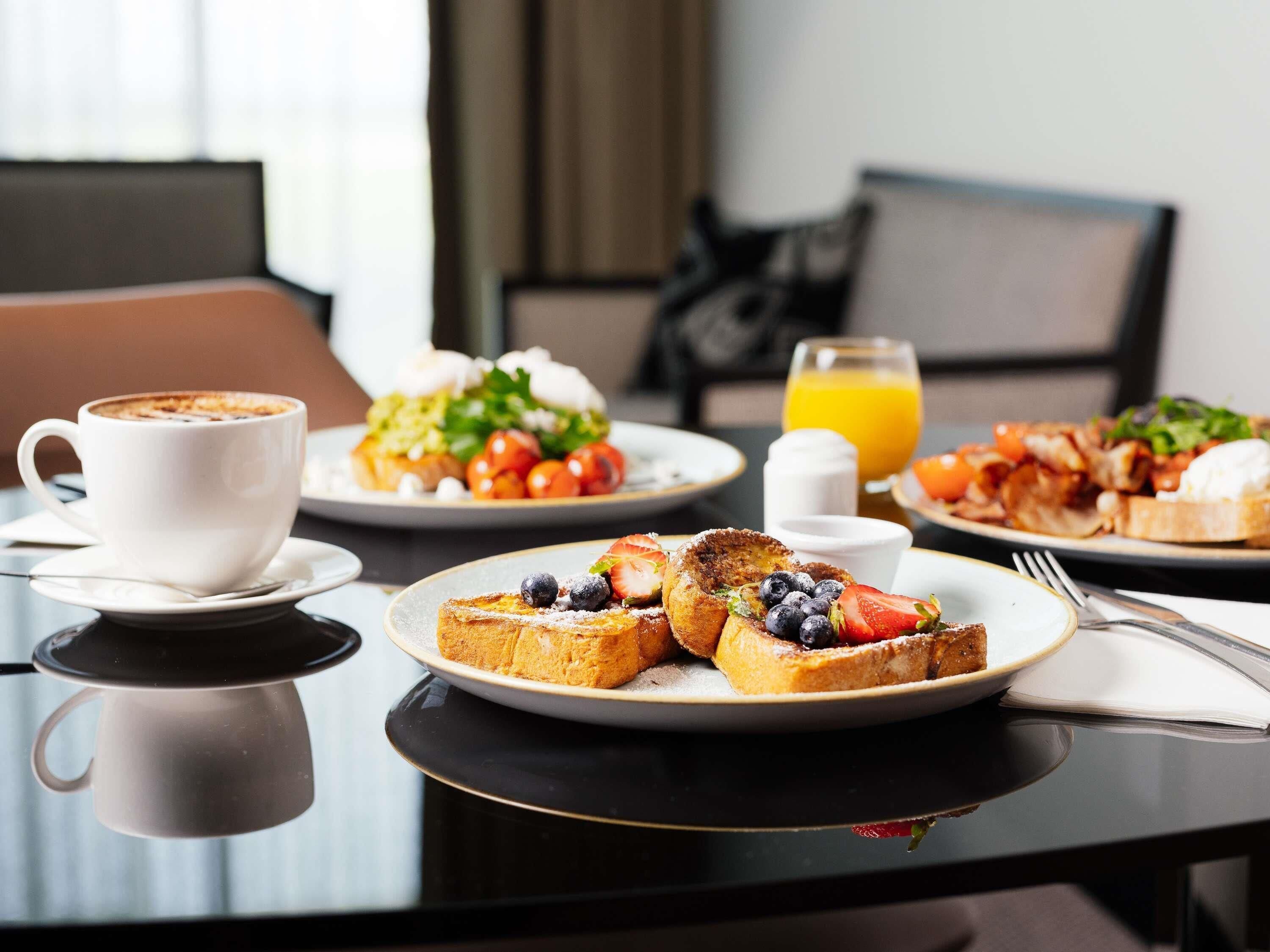 A breakfast setting with a cup of coffee, toast with berries, a plate of eggs, tomatoes, and a glass of orange juice.