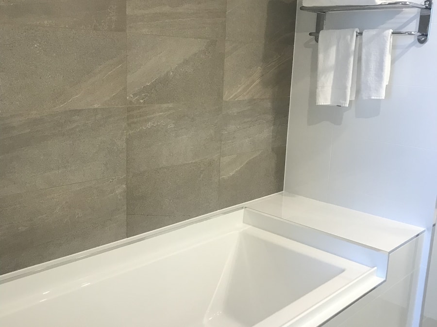 Un baño moderno con una bañera blanca grande, paredes de azulejos grises y un perchero con toallas dobladas.