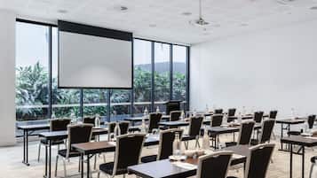 A conference room with a large screen, tables, chairs, and a view of greenery outside.