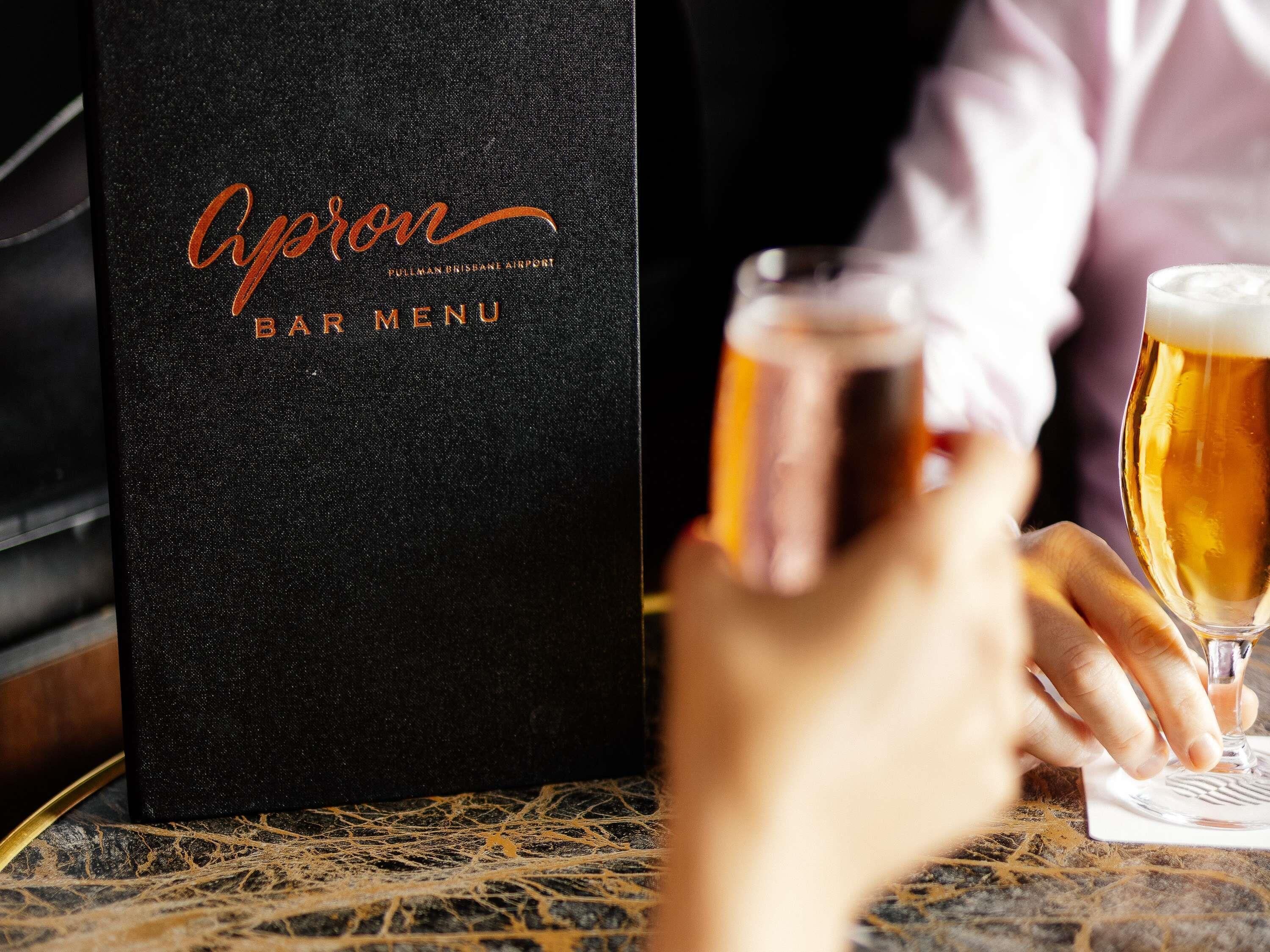 A black bar menu with 'Apton' and 'BAR MENU' text, a glass of beer, and a hand holding a coaster.