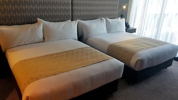 Ein Hotelzimmer mit zwei Betten, einem gemusterten Kopfteil, einem Nachttisch mit Lampe und einem Fenster mit Vorhängen.