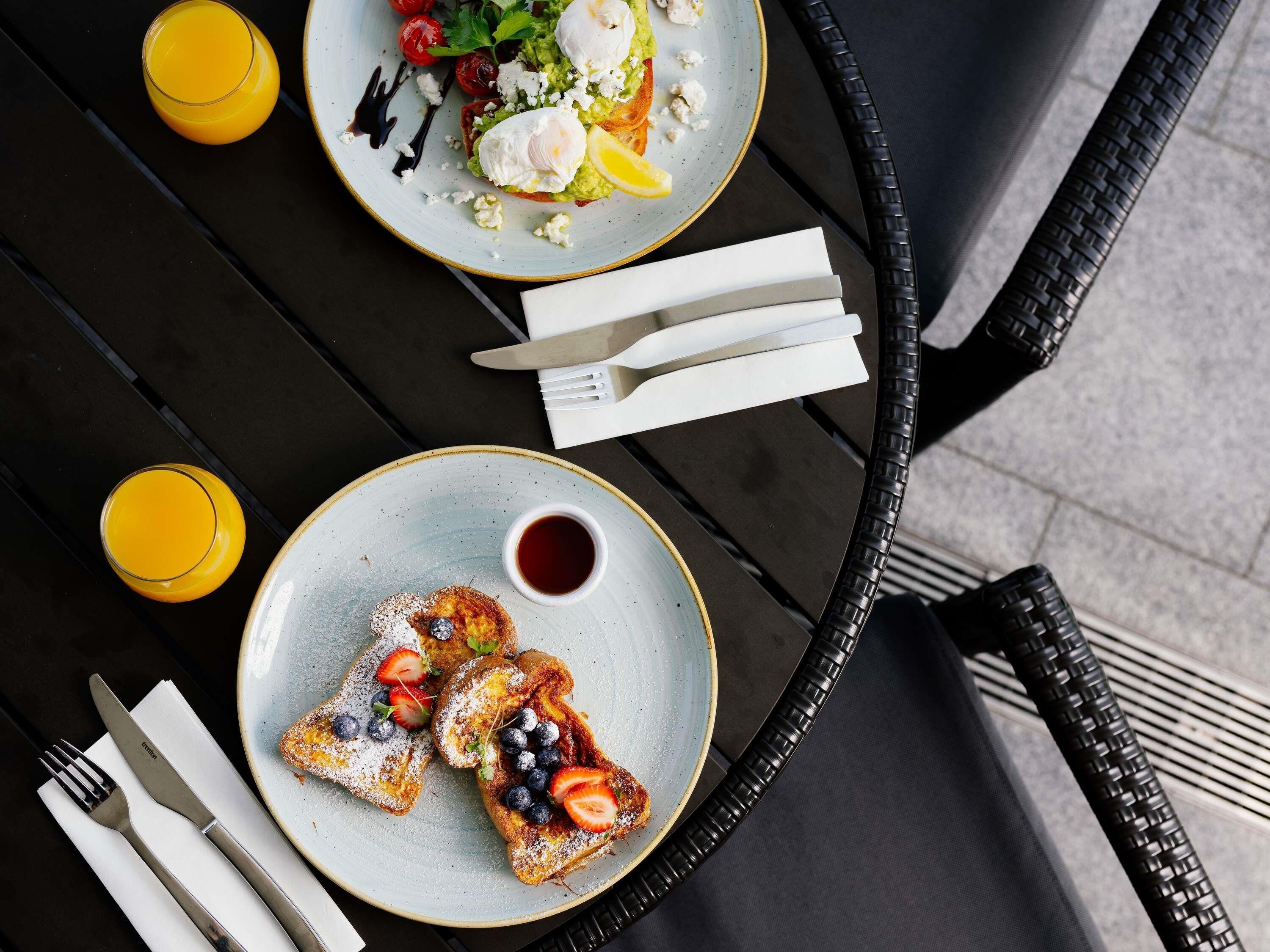 A table with breakfast items including toast with berries and a poached egg, a plate with a salad and poached egg, and two glasses of orange juice.