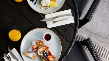 A table with breakfast items including toast with berries and a poached egg, a plate with a salad and poached egg, and two glasses of orange juice.