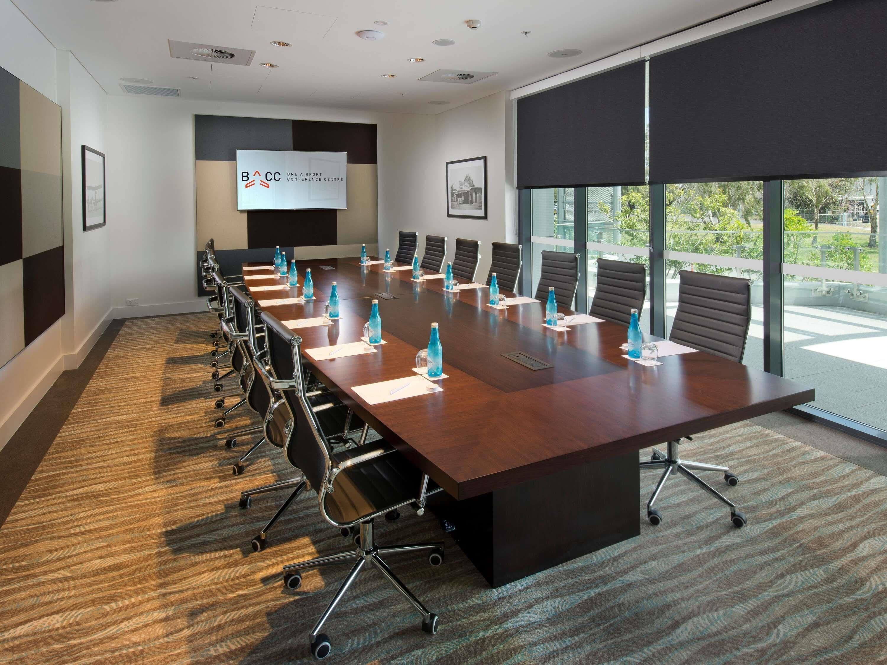 A conference room with a long table, chairs, a projector screen, and a large window.