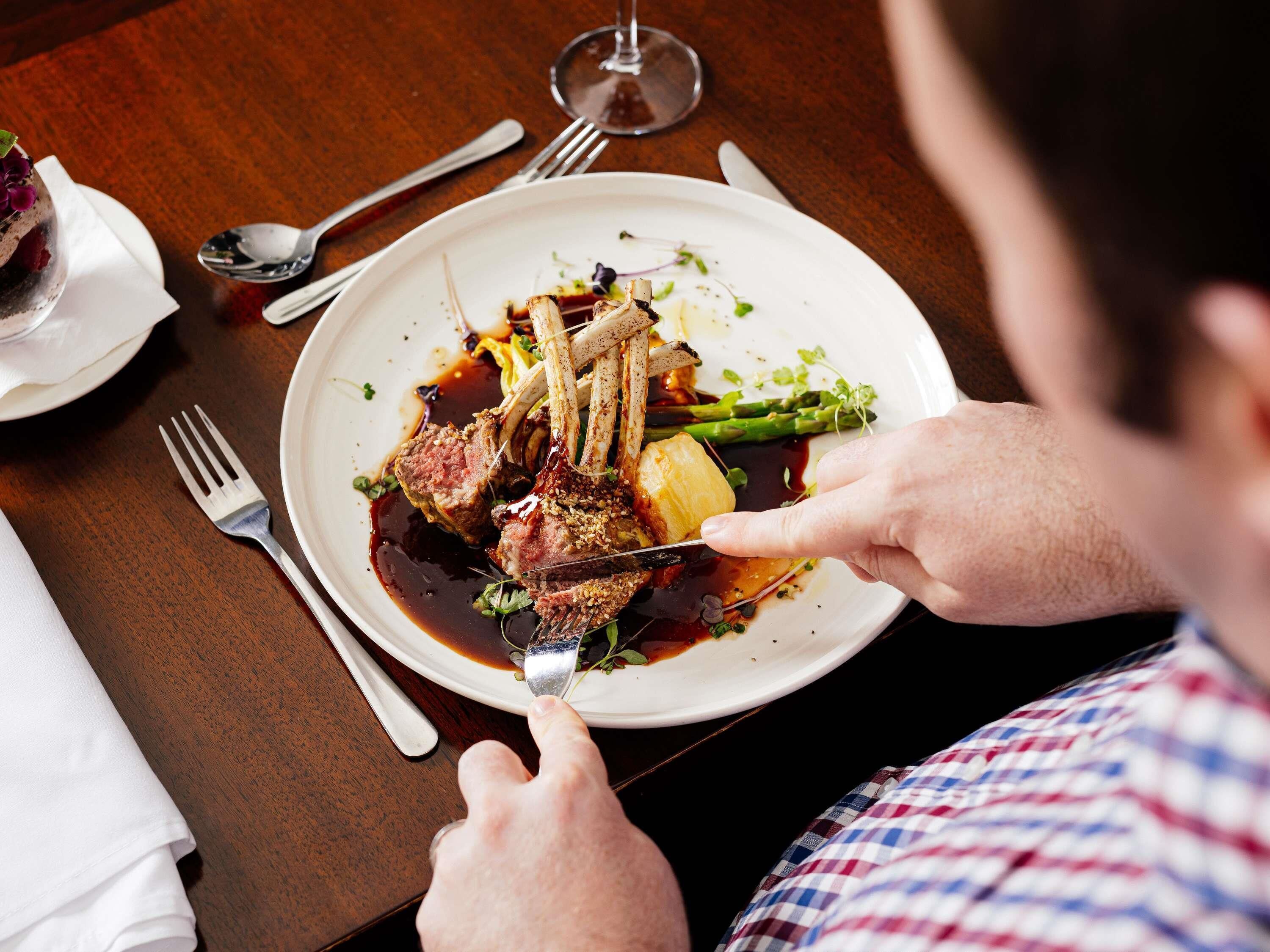 A person dining at a table with a plate of food, a fork, and a spoon.