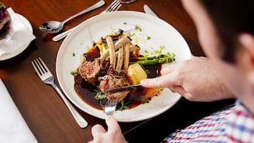 A person dining at a table with a plate of food, a fork, and a spoon.