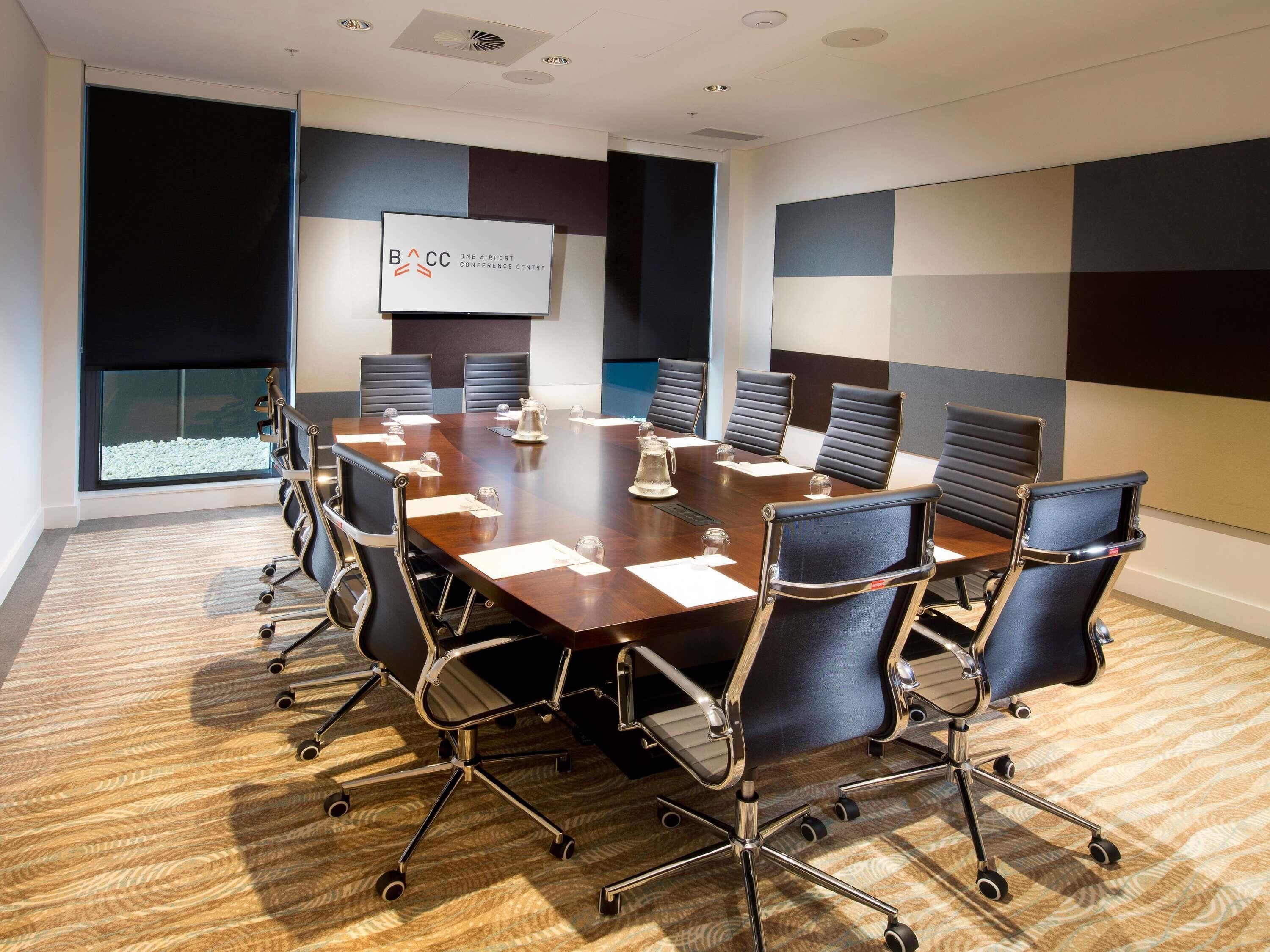 A conference room with a large table, chairs, a projector screen, and a view of the outdoors.