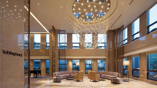 A spacious lobby with a grand chandelier, a piano, and comfortable seating areas.