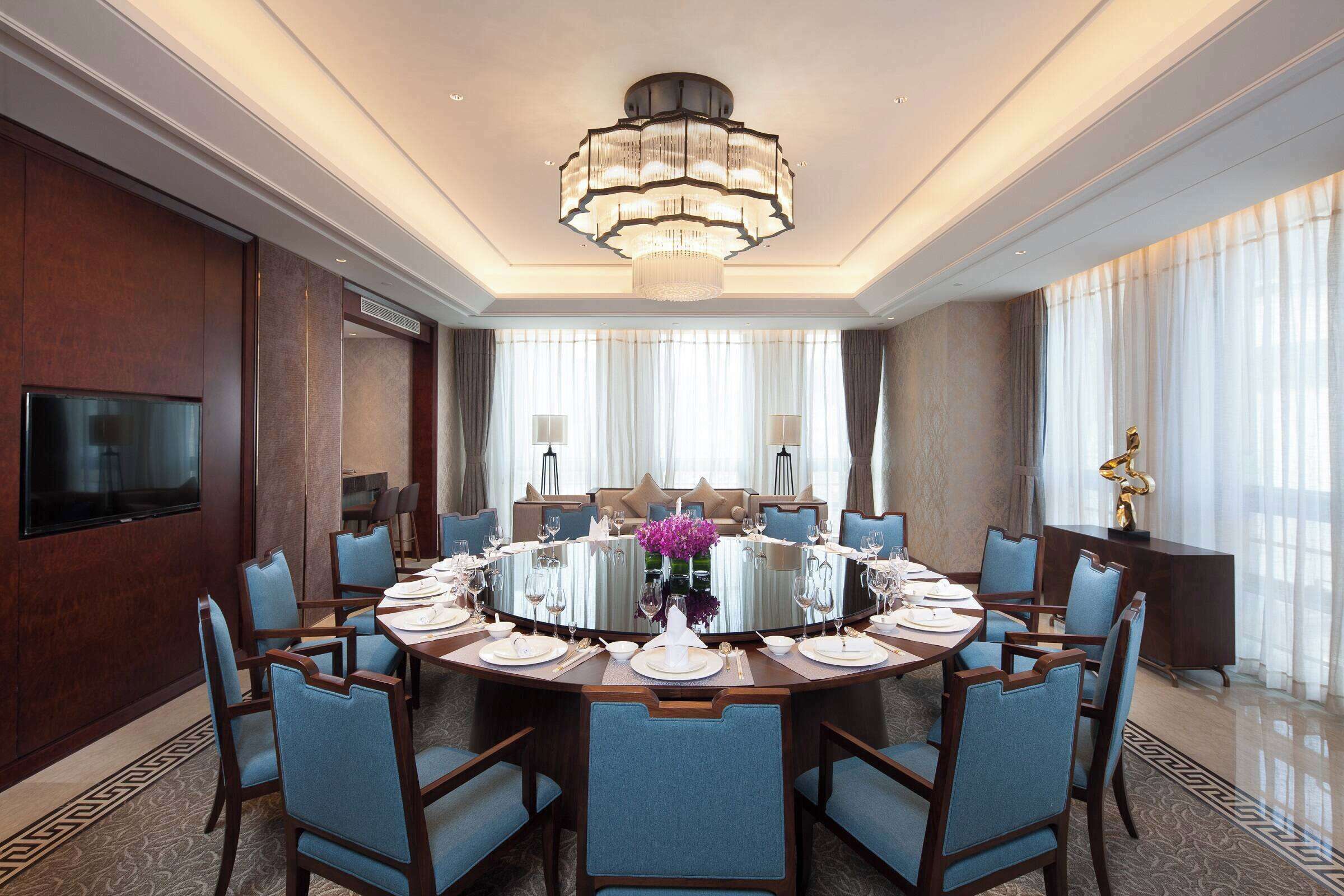 A spacious dining area with a round table, blue upholstered chairs, and a large chandelier.