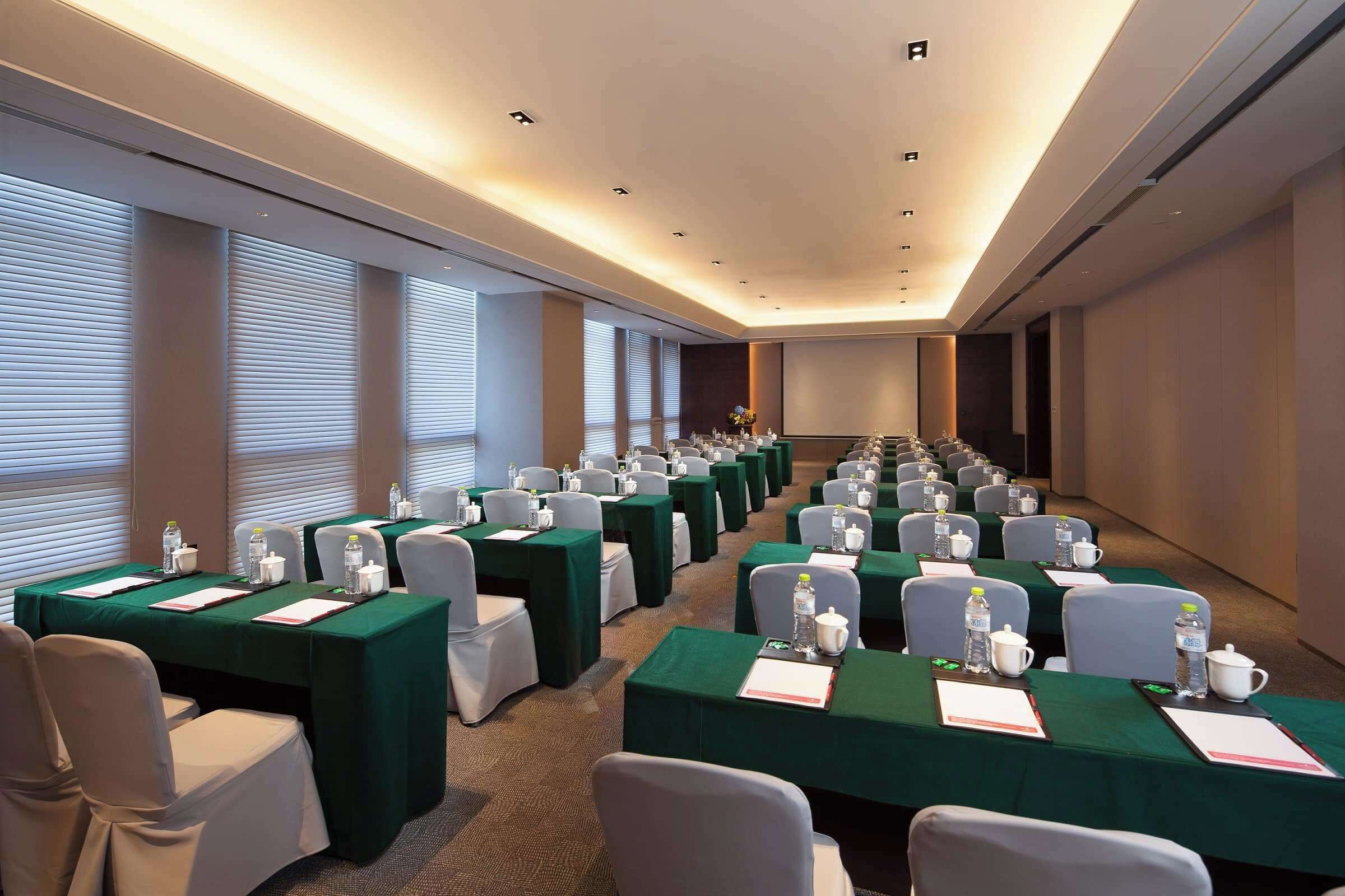 A conference room with rows of tables, each with a green tablecloth, white chairs, and water bottles.