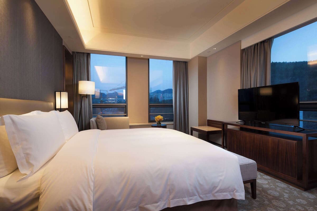 A hotel room with a large bed, a TV, a desk, and a view of the cityscape.