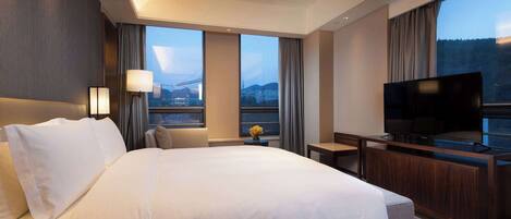 A hotel room with a large bed, a TV, a desk, and a view of the cityscape.