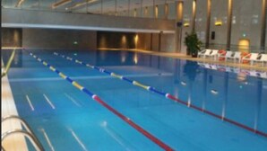 An indoor swimming pool with lane dividers, lounge chairs, and a modern architectural design.