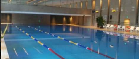 An indoor swimming pool with lane dividers, lounge chairs, and a modern architectural design.