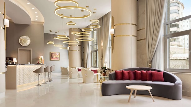 Een moderne hotellobby met een gebogen bank, een ronde tafel en een bar met krukken.