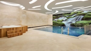 Een moderne spa met een groot binnenzwembad, houten banken en een wanddecoratie met een waterval.