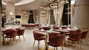 Een modern restaurant met ronde tafels, rode stoelen en ronde plafondlampen.