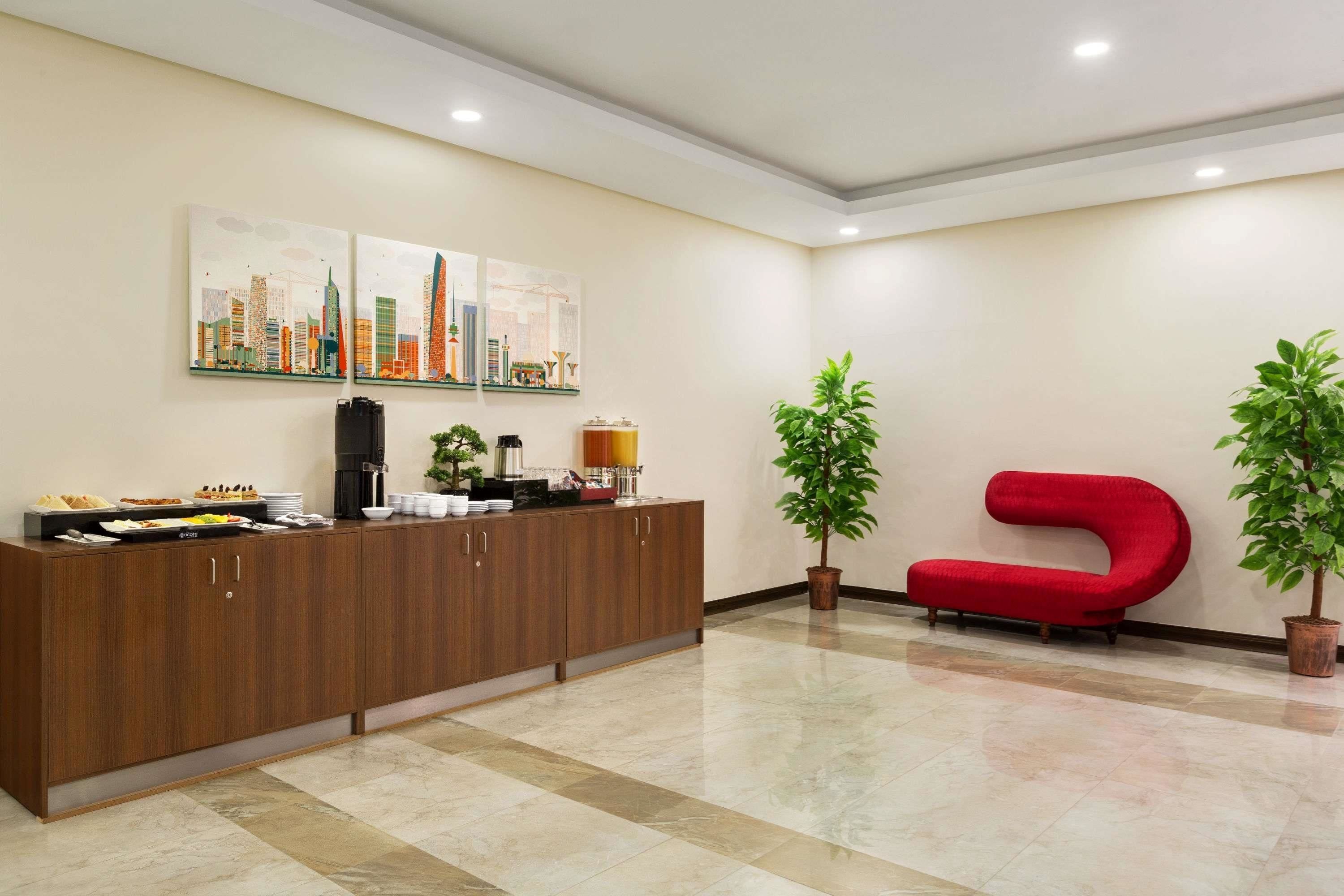 Una zona de recepción con un mostrador de madera, un sillón tapizado de color rojo y dos plantas en macetas.