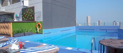 Una piscina en la azotea con sillones de descanso, un flotador salvavidas y vistas del horizonte de la ciudad.