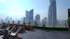 Terraza en la azotea con sillones y mesas, con vistas a un horizonte urbano de rascacielos modernos.