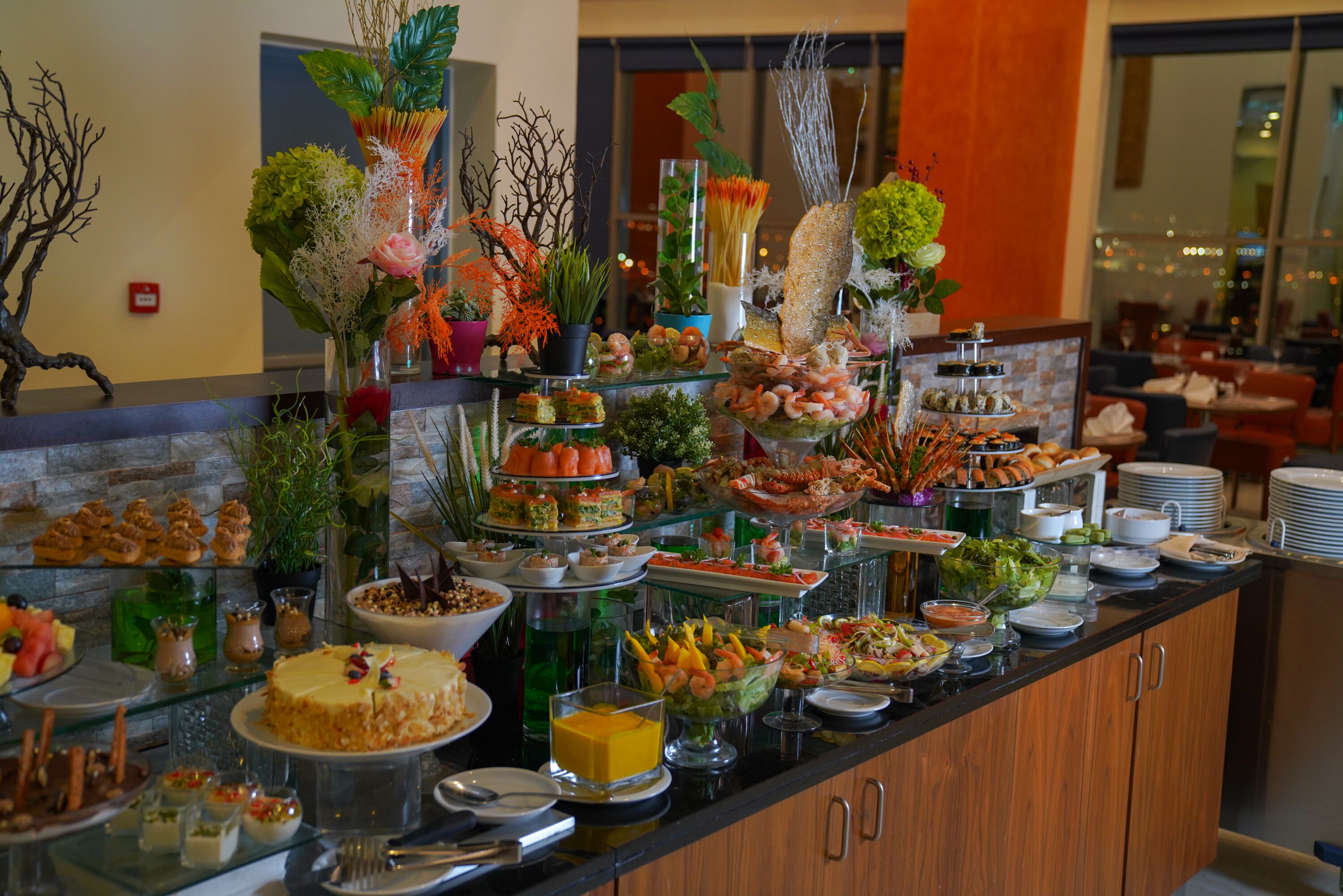 A buffet with various food items and decorative plants.