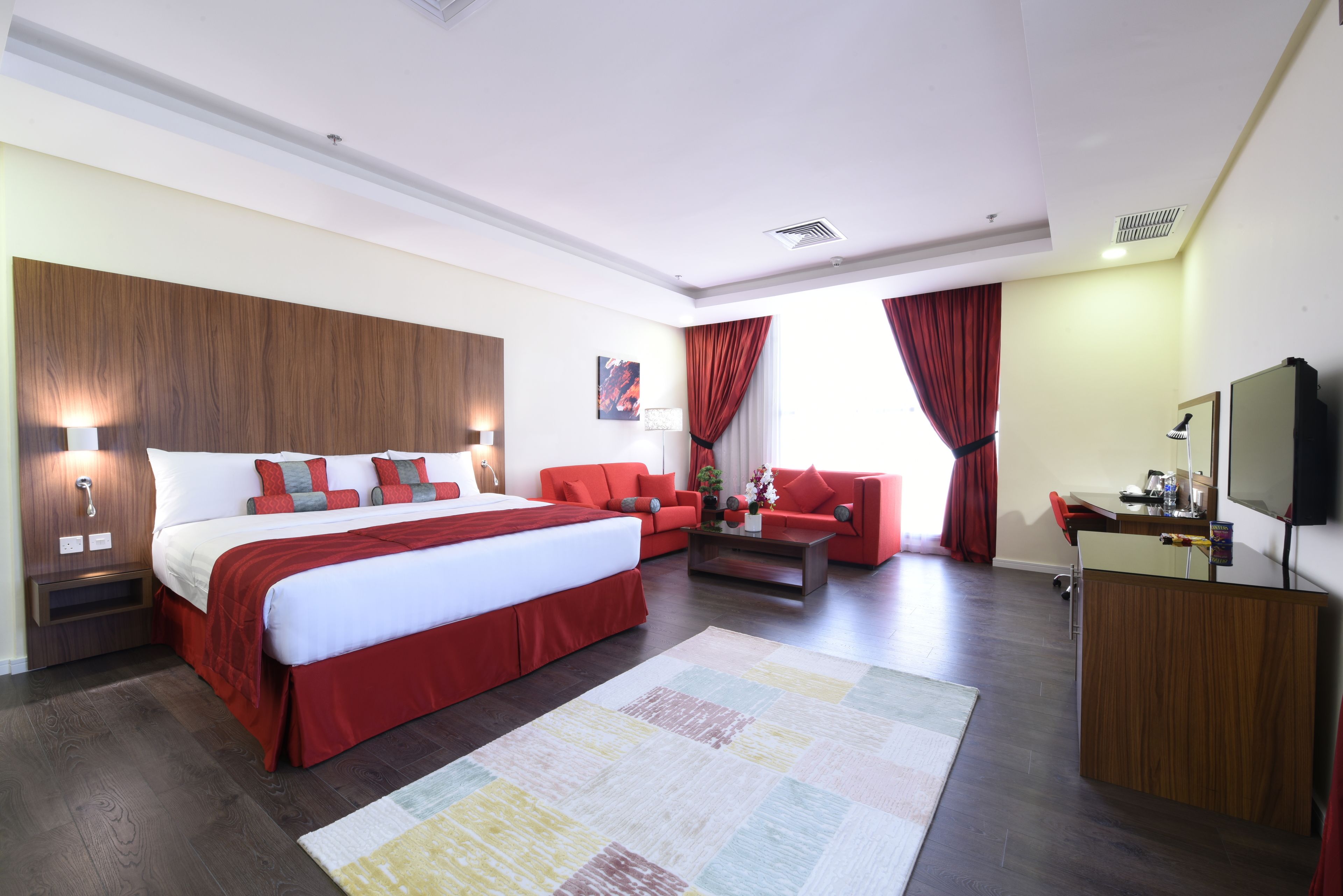 A hotel room with a large bed, a sofa, a coffee table, and a TV.